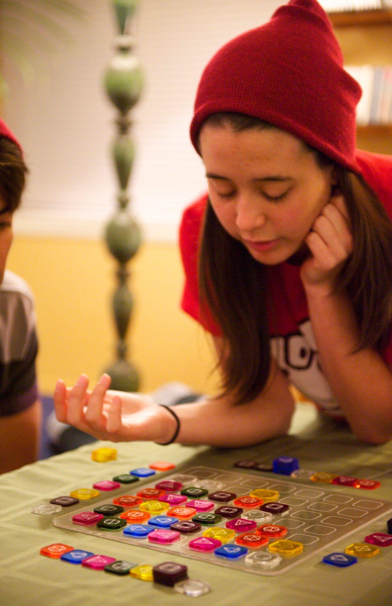 There is a light skinned person looking down that seems to be thinking. They are looking at a clear board filled with colorful square tokens arranged in a particular pattern.