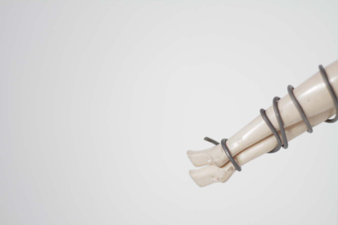 There are two light skinned doll legs wrapped together by a gray wire like material.
