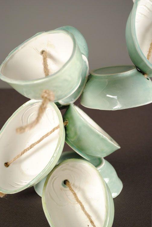 There are light green oval ceramic bowls with holes in them connected with twine. The shape is abstract and not in any particular way.
