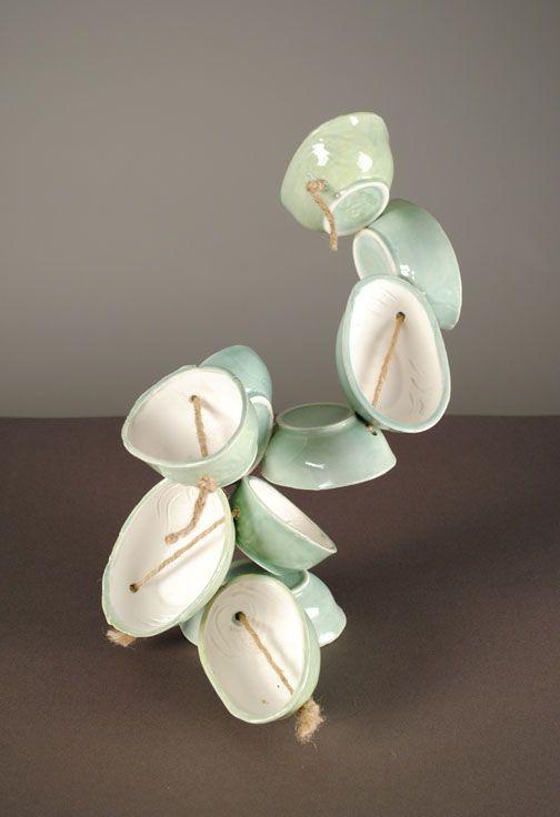 There are light green oval ceramic bowls with holes in them connected with twine. The shape is abstract and going vertically.