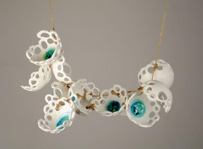 There is an arrangement of white bowl like objects with lots of holes on the edges connected with twine. The overall shape looks like a curve. Inside each of the bowls is blue or green paint on the very bottom.