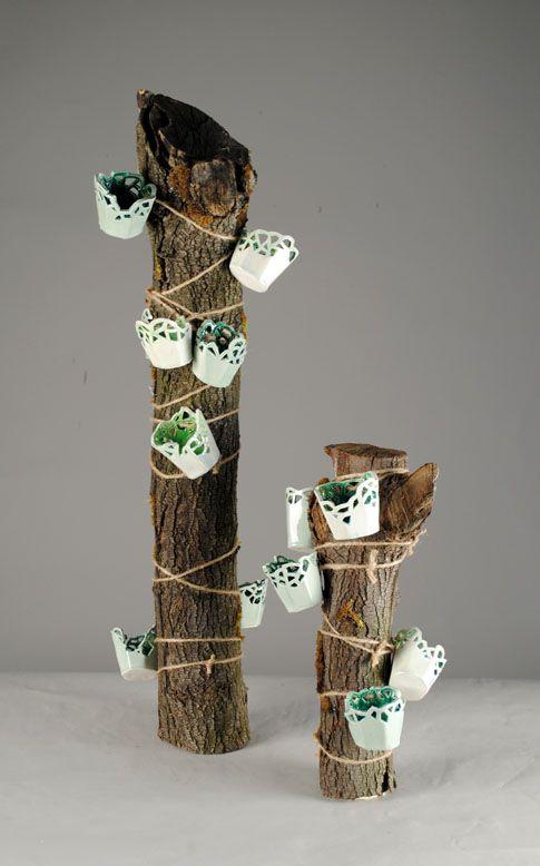 There are two pieces of wood wrapped with twine and little white baskets. The baskets are connected by the twine and have a white exterior and green interior. The background is gray.