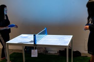 People playing ping pong on a ping pong table with an overhead projection.