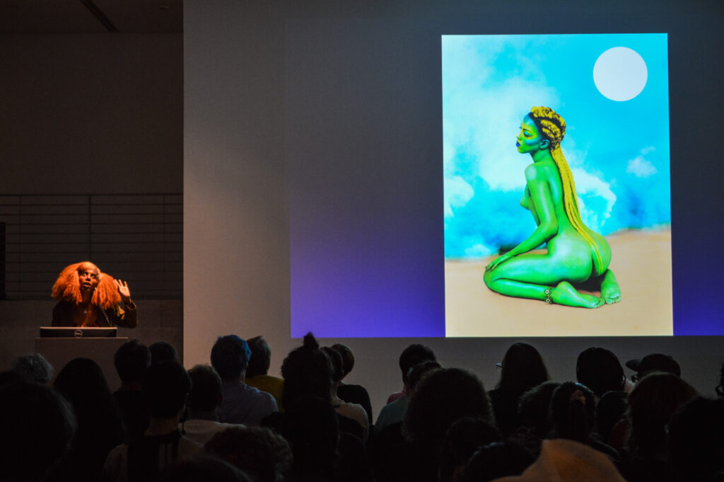 JULIANA HUXTABLE is standing next to a painting being projected in the EDA pit.