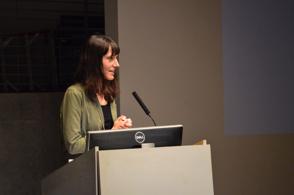 Astra taylor is speaking at a pedestal.