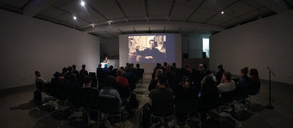 Wide shot of a crowd sitting in front of Astra Taylor.