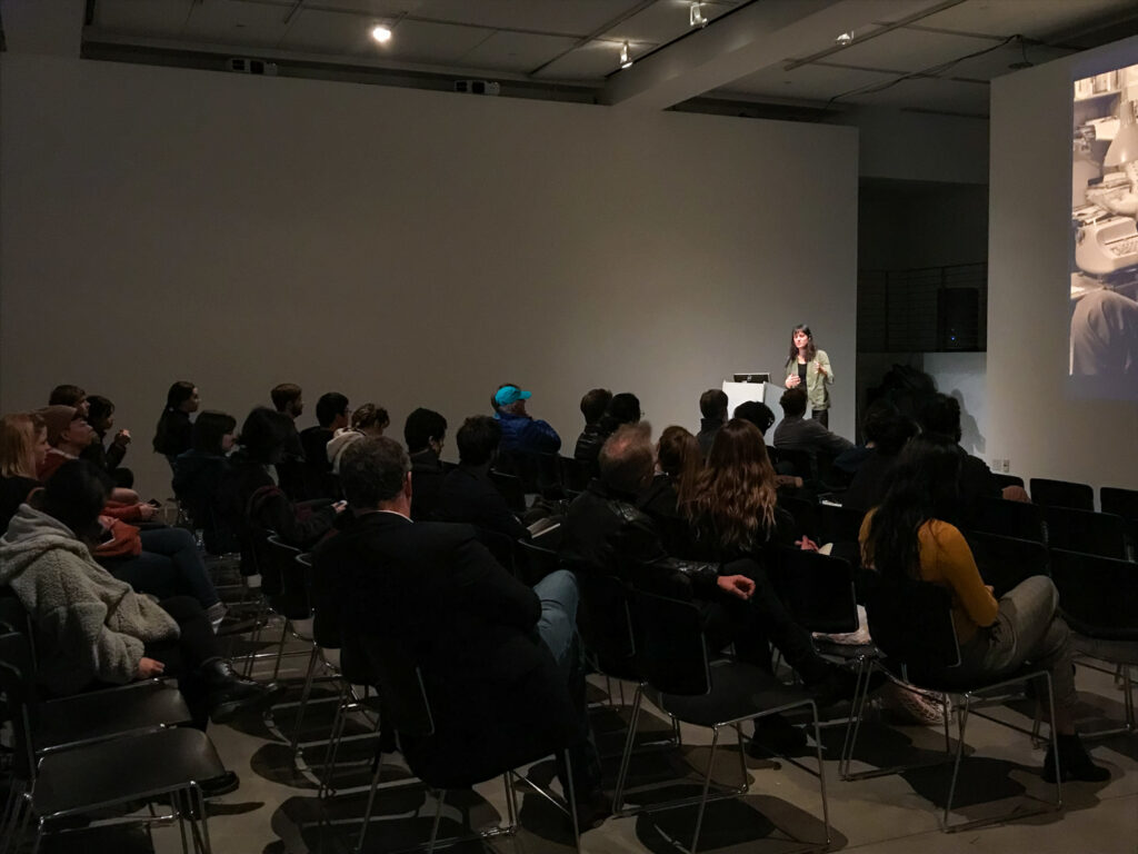 Wide shot of a crowd sitting in front of Astra Taylor.