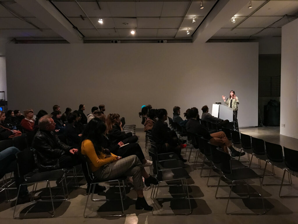 Wide shot of a crowd sitting in front of Astra Taylor.