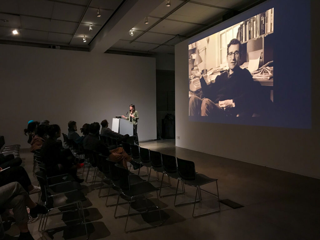 Wide shot of a crowd sitting in front of Astra Taylor.