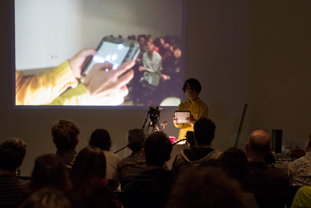 Toshio Iwai is holding some sort of handheld LED lit controller.