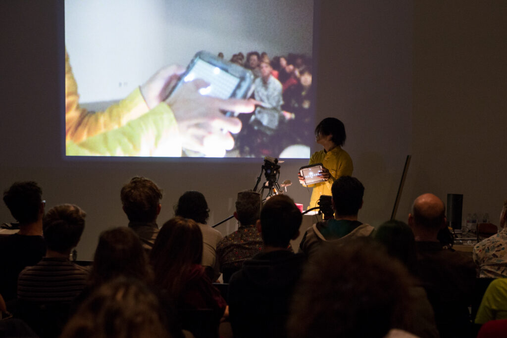 Toshio Iwai is holding some sort of handheld LED lit controller.