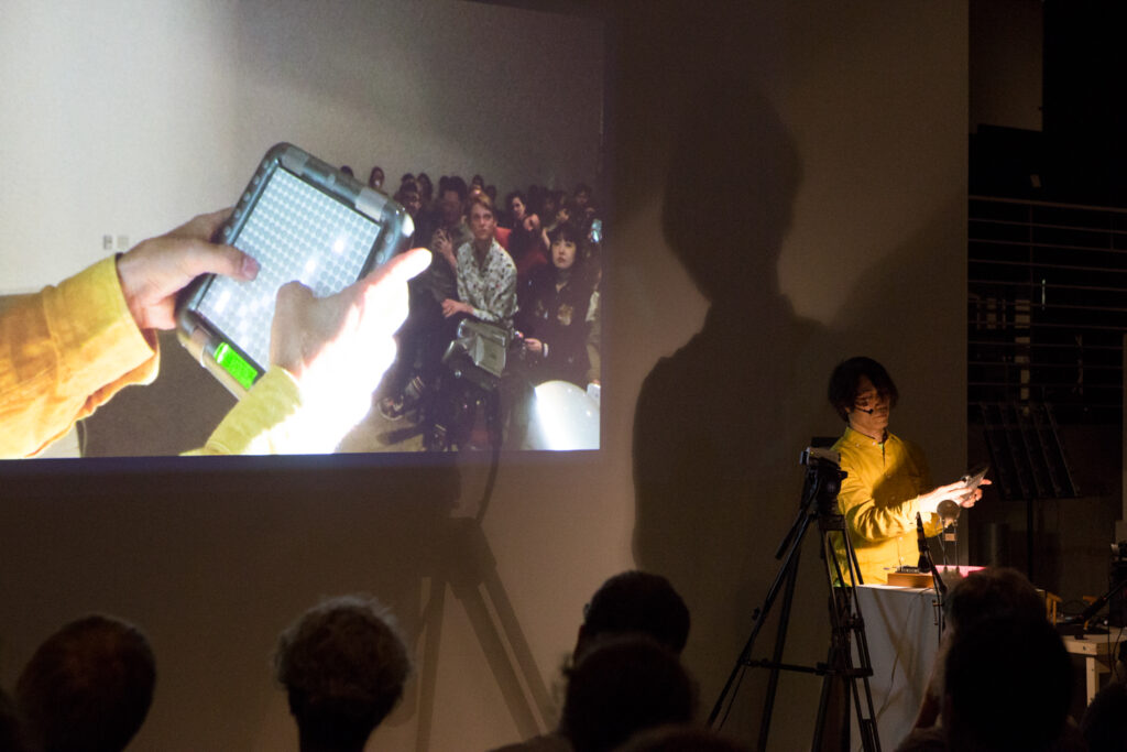 Toshio Iwai is holding some sort of handheld LED lit controller.