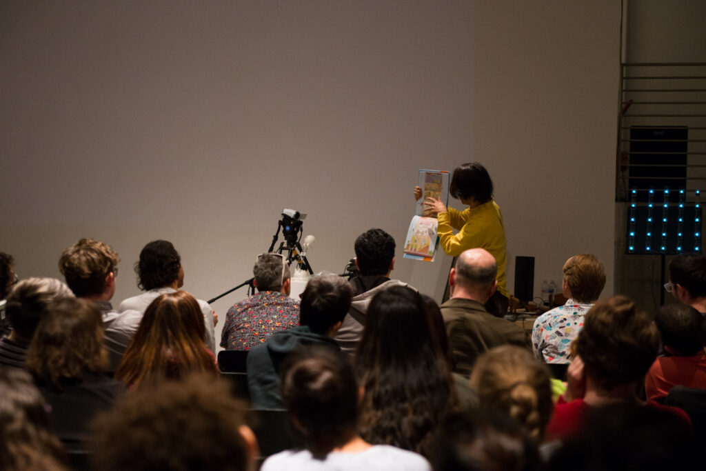 Toshio Iwai holding a picture book for the audience in the EDA pit.