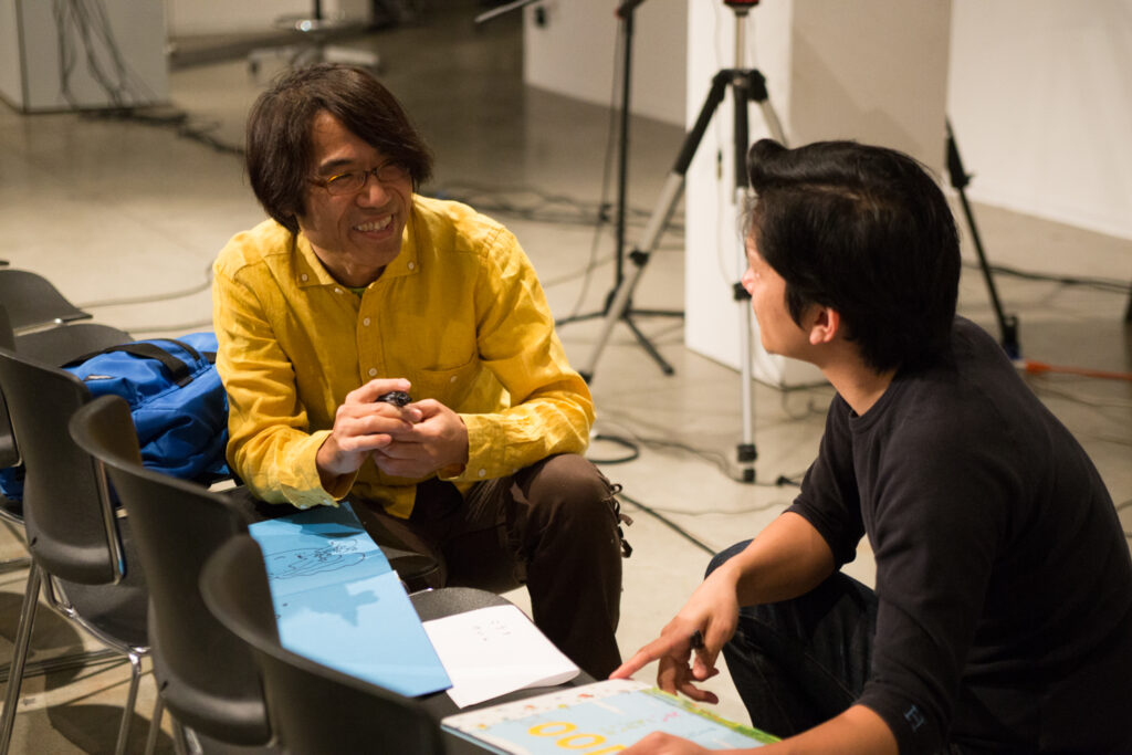 Toshio Iwai is drawing a picture on blue paper.