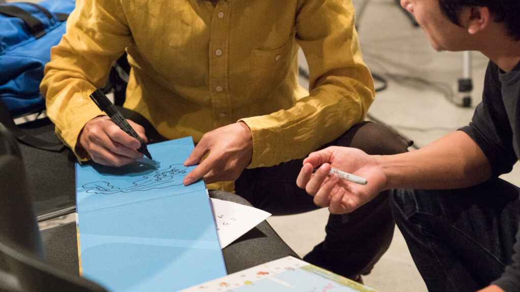 Toshio Iwai is drawing a picture on blue paper.