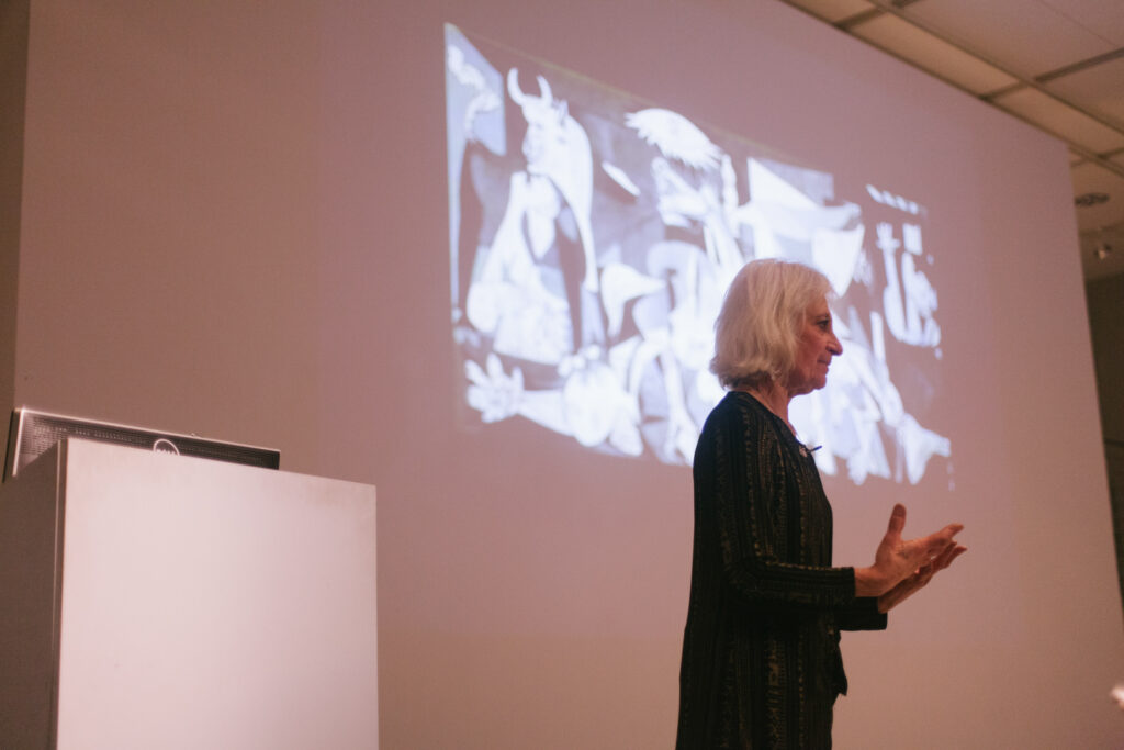 Linda Weintraub is gesturing in front of her power point slide.