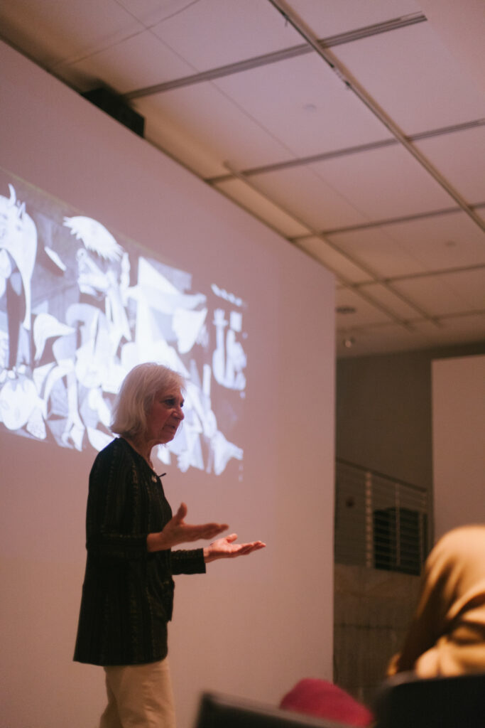 Linda Weintraub is gesturing in front of her power point slide.