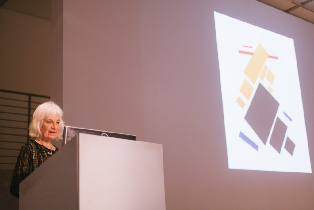 Lina Weintraub's lecture presentation. Lina is showing graphics of red, black, and blue rectangles being projected on the EDA walls.