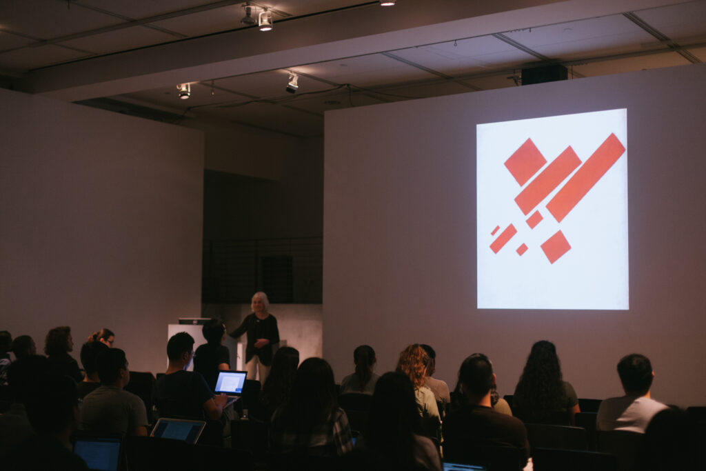 Lina Weintraub's lecture presentation. Lina is showing graphics of red rectangles being projected on the EDA walls.