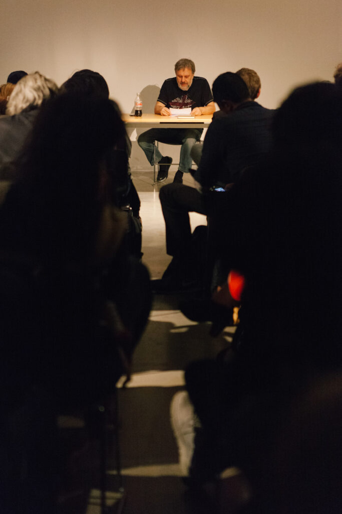 Zizek looking down at papers in front of an audience in the EDA pit.