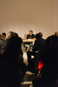 Zizek talking at a desk in front of an audience in the EDA pit.