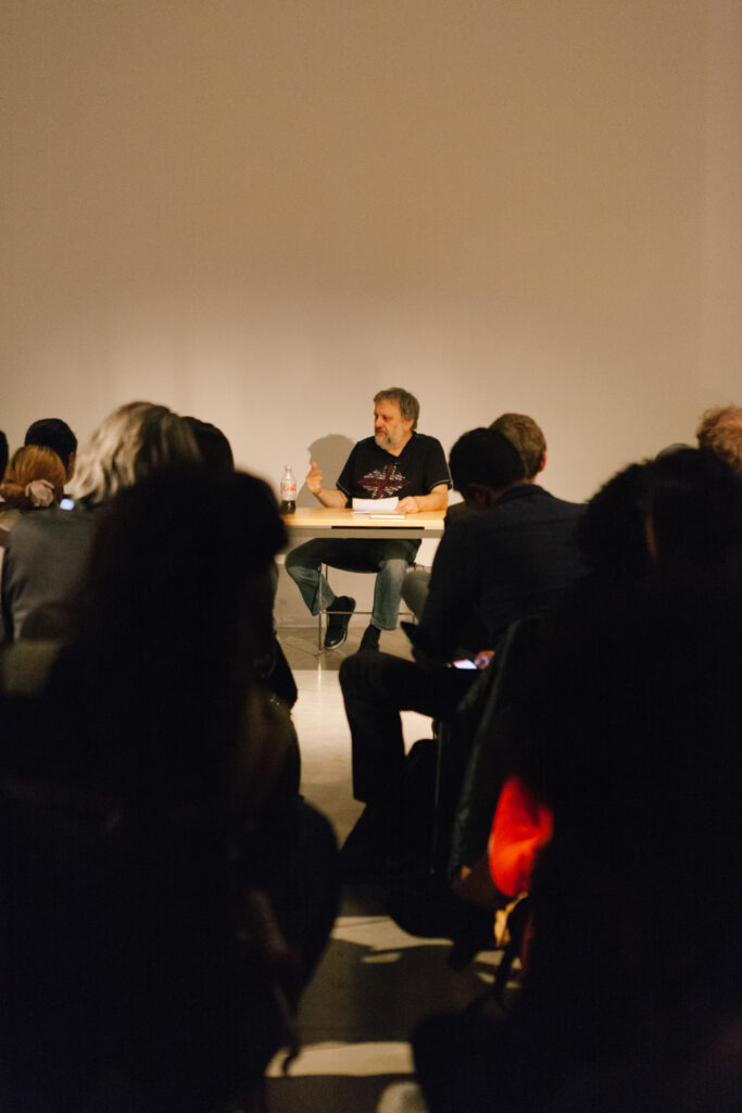 Zizek talking at a desk in front of an audience in the EDA pit.