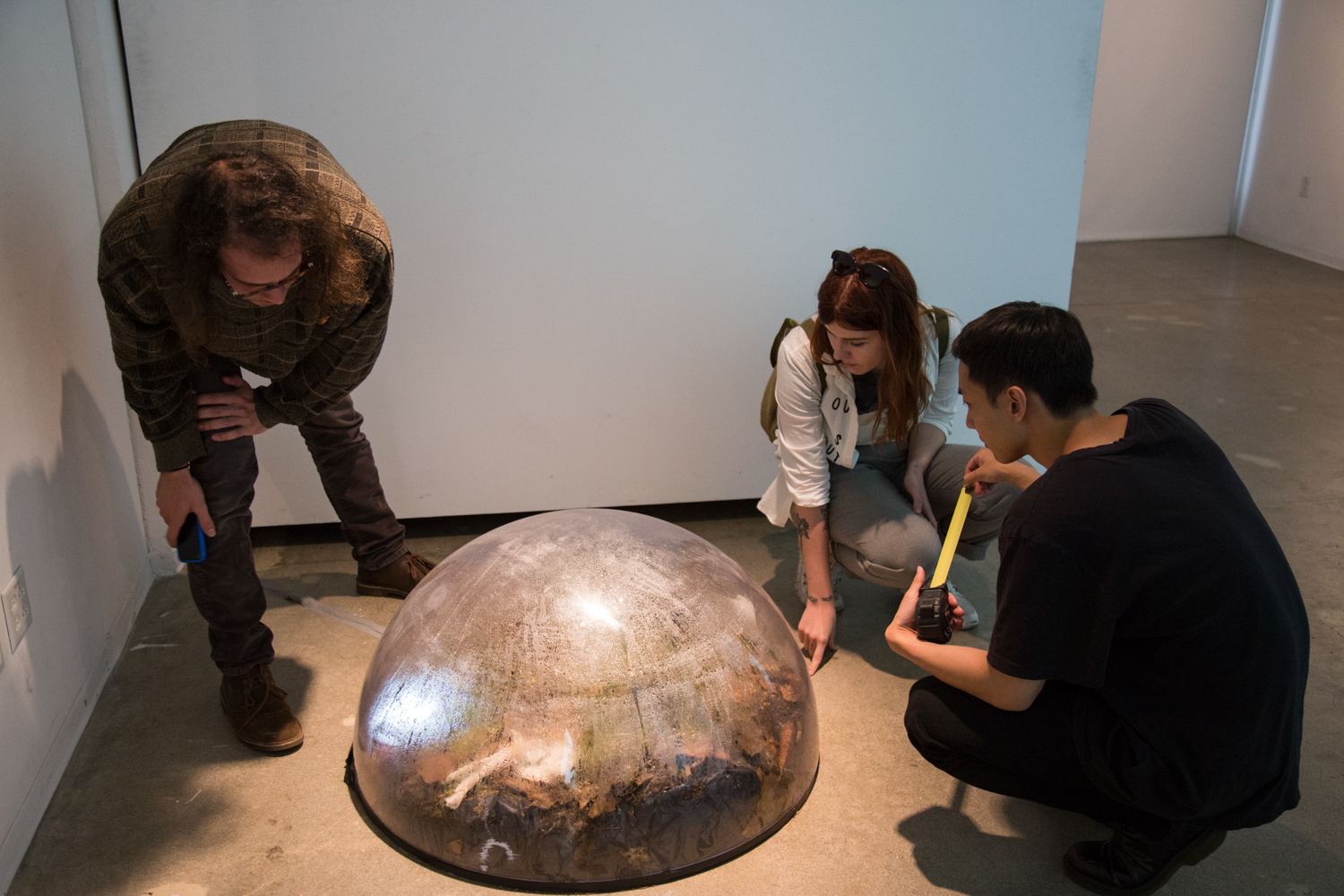 3 people inspecting Maru Garcia's sculpture work on the floor.