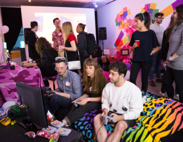 People crowded around a tv monitor, playing a game. The tv monitor is on the floor and the people are sat on a zebra print throw blanket.