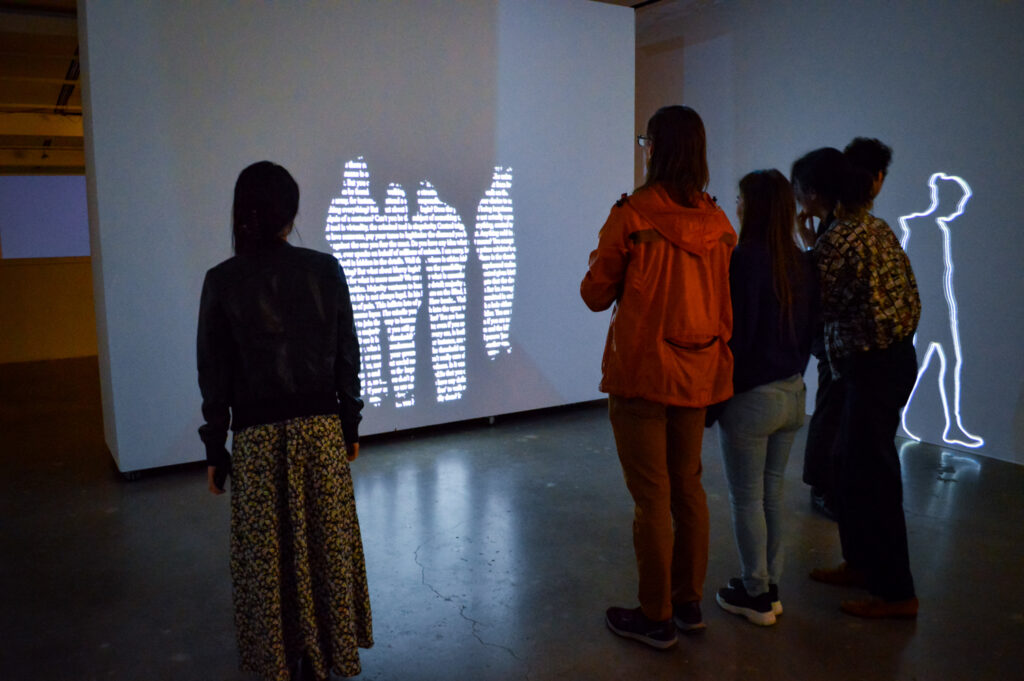 ZEYNEP ABES projection of people on a wall. There is text within the people being projected.