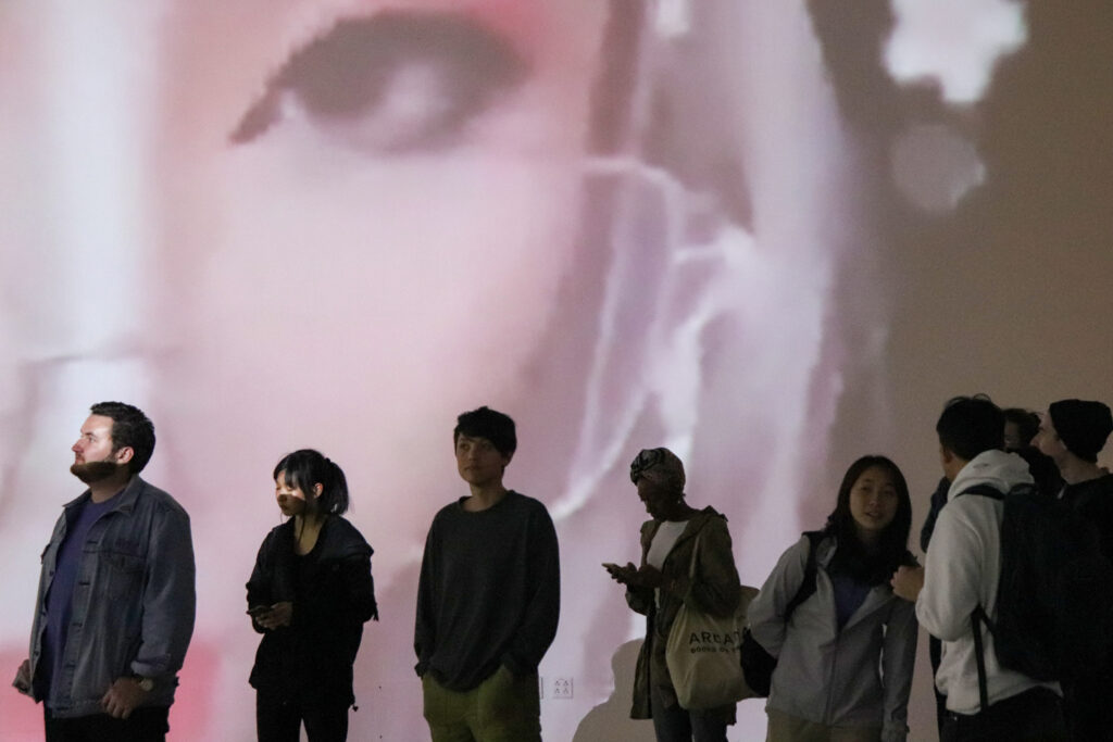 People standing in front of Zheng Fang's projection work in the EDA pit. The projection is of a twitch streamer's eye.