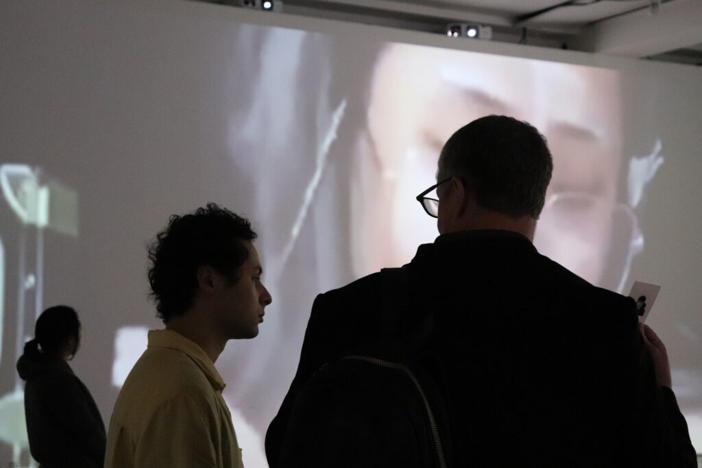 People talking in front of Zheng Fang's projection work.