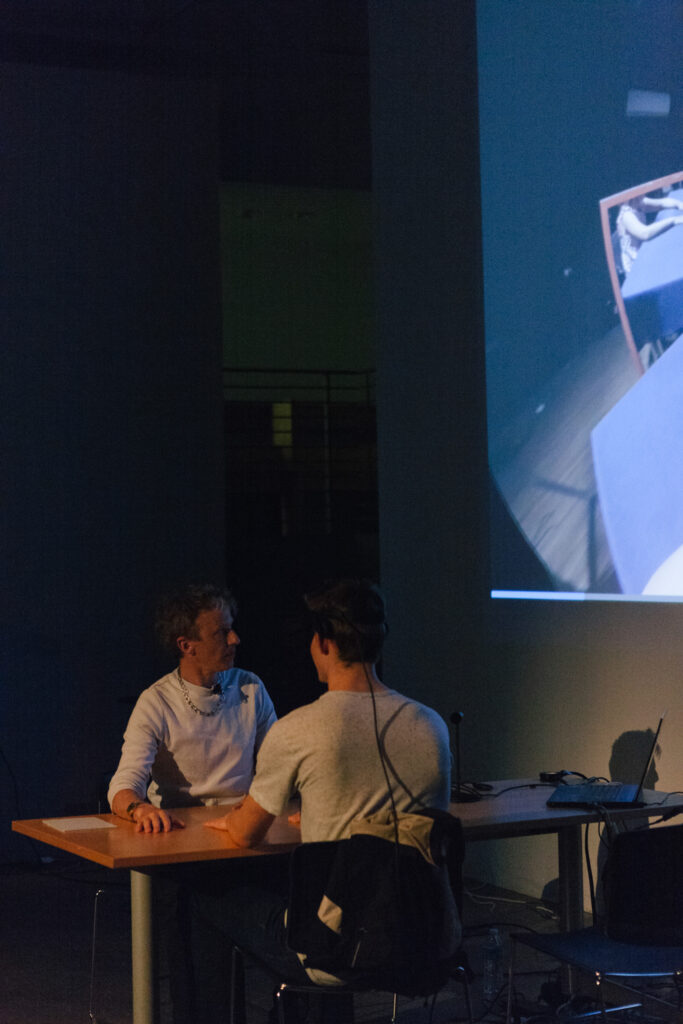 Person is wearing a VR headset and holding their hands out to another person on a desk.