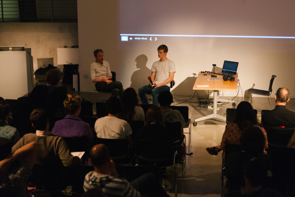 Daniel Landau's lecture in the EDA pit. Two people are lit sitting in chairs in front of the EDA pit center wall.