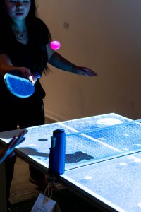 Person playing ping pong on a ping pong table with an overhead projection.