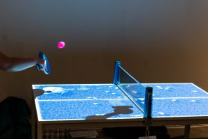 Person playing ping pong on a ping pong table with an overhead projection.
