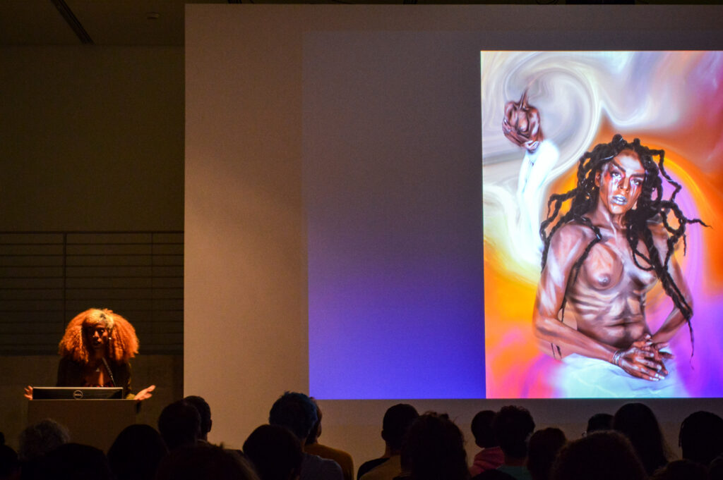 JULIANA HUXTABLE is standing next to a painting being projected in the EDA pit.