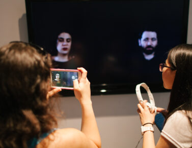 Person taking a photo of two people being displayed on a tv monitor.