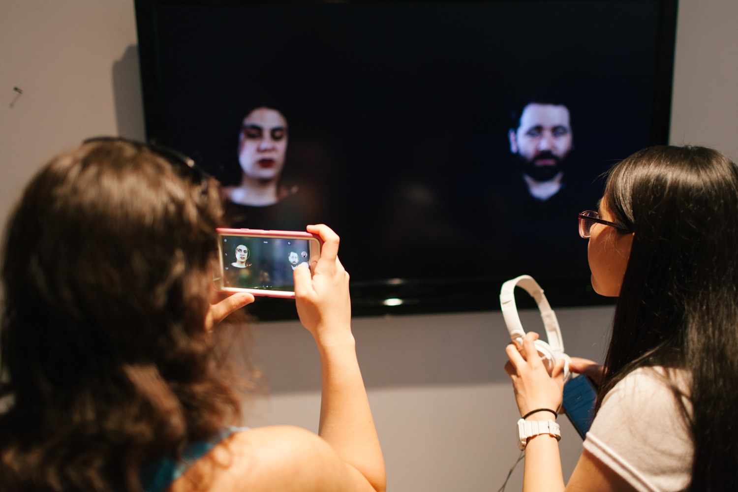 Person taking a photo of two people being displayed on a tv monitor.
