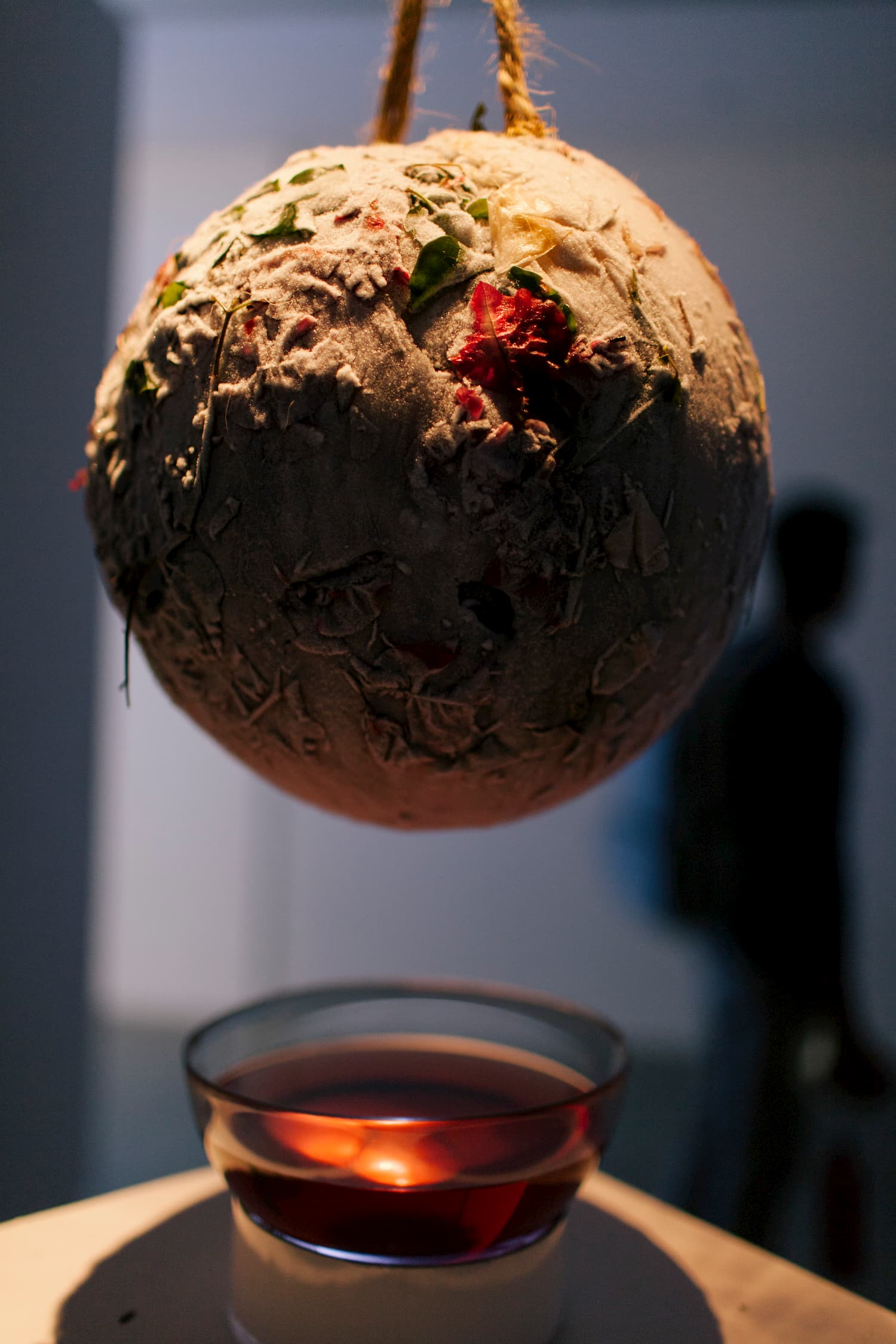 Sphere hanging by a style of thread over a pan of water. Joteva's solo show.