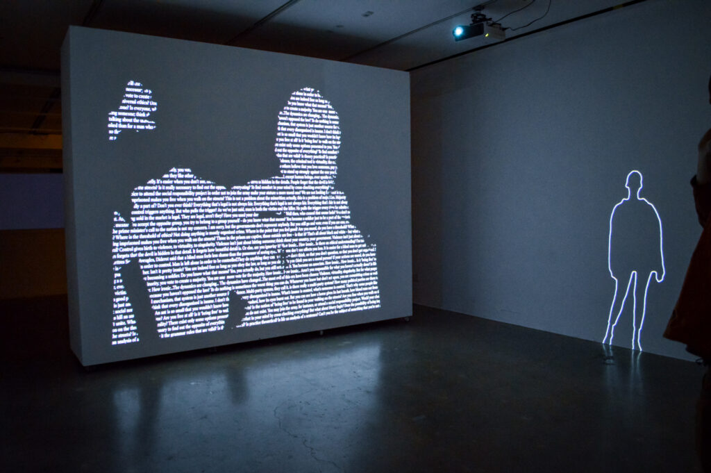 ZEYNEP ABES projection of people on a wall. There is text within the people being projected.