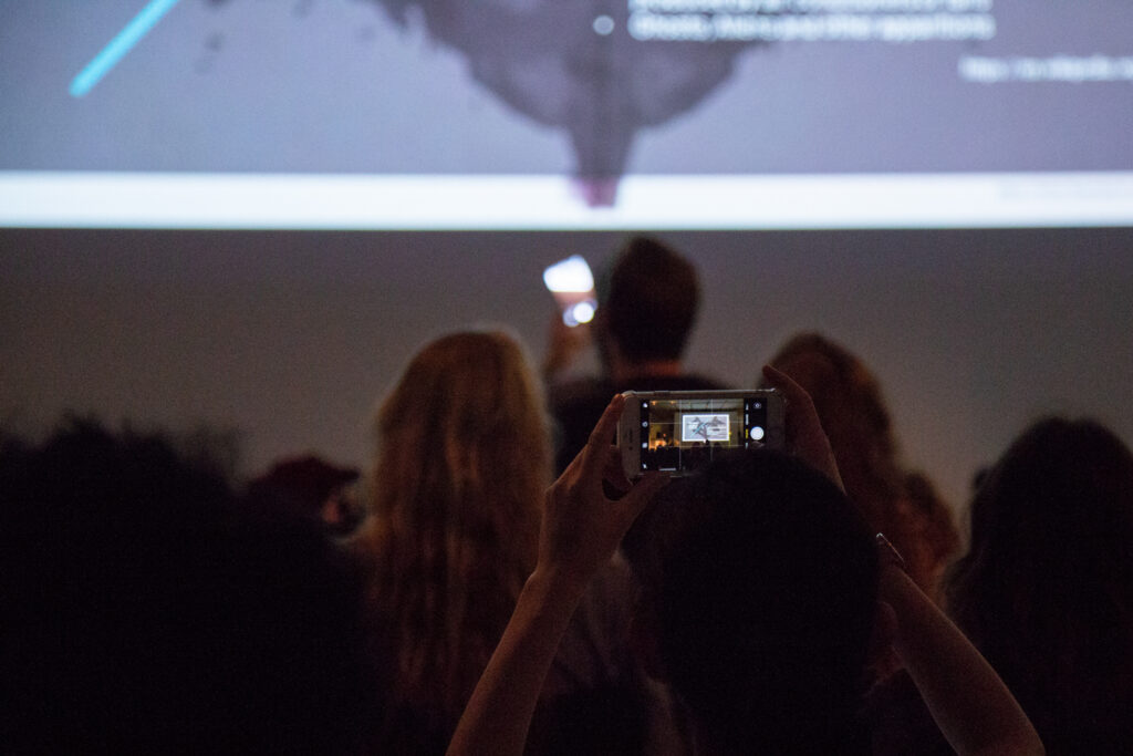 Audience member taking a picture of a projected slide with their phone.
