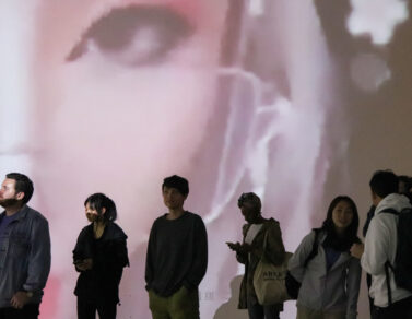 People standing in front of Zheng Fang's projection work in the EDA pit. The projection is of a twitch streamer's eye.