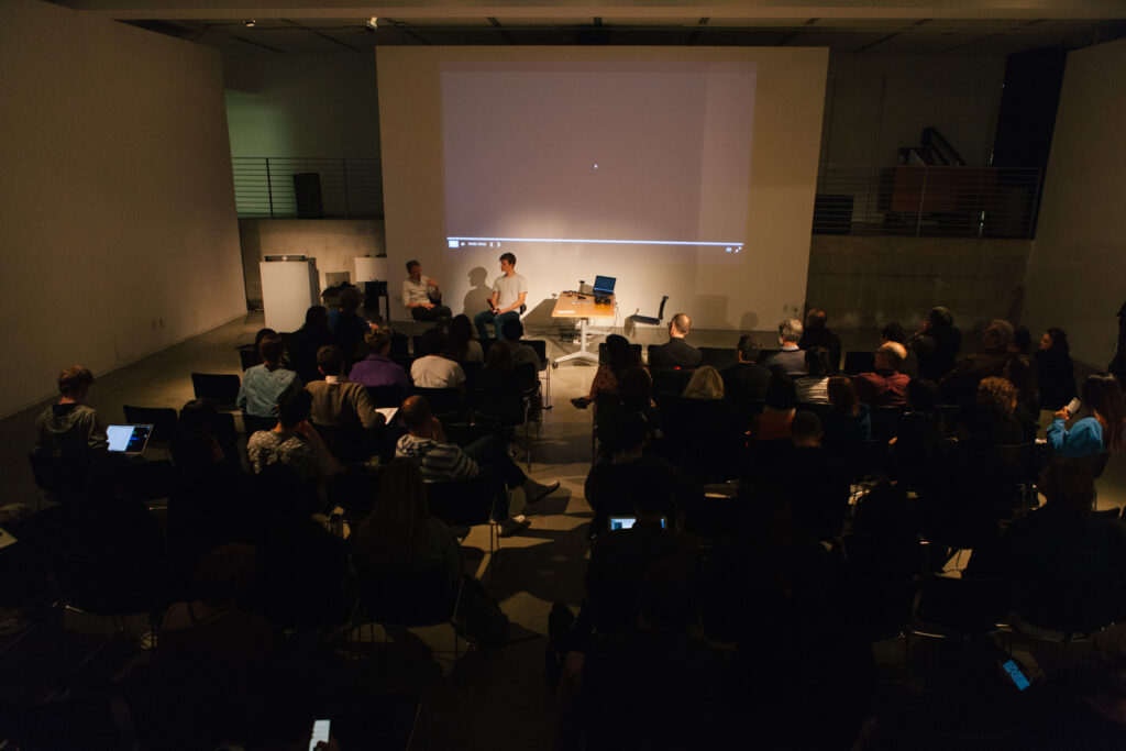 Daniel Landau's lecture in the EDA pit. Two people are lit sitting in chairs in front of the EDA pit center wall.